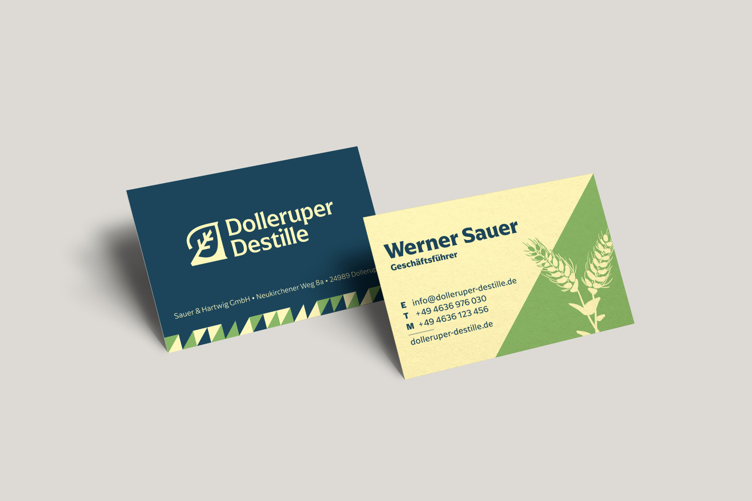 Mockup zweier Visitenkarten: die Vorderseite mit Logo auf dunkelblauem Grund, die Rückseite mit Kontaktdaten und einer Illustration von Getreideähren.
